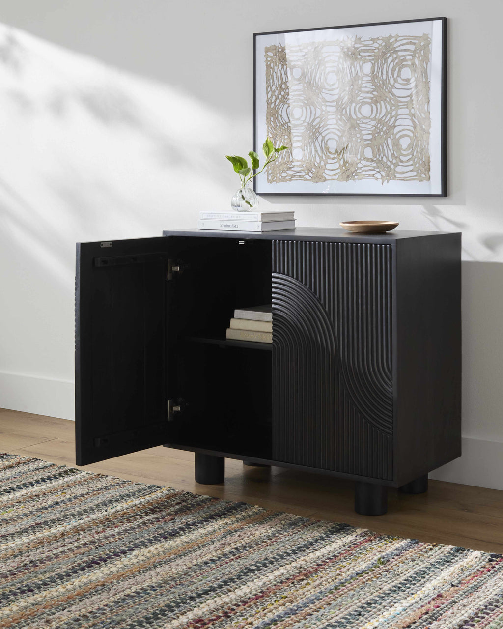 Black sideboard with open drawer in a room with a rug and framed artwork on the wall.