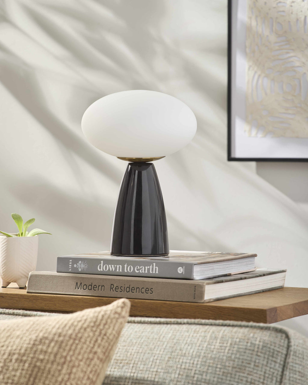 Contemporary table lamp with a black base and white shade on top of books on a wooden surface.