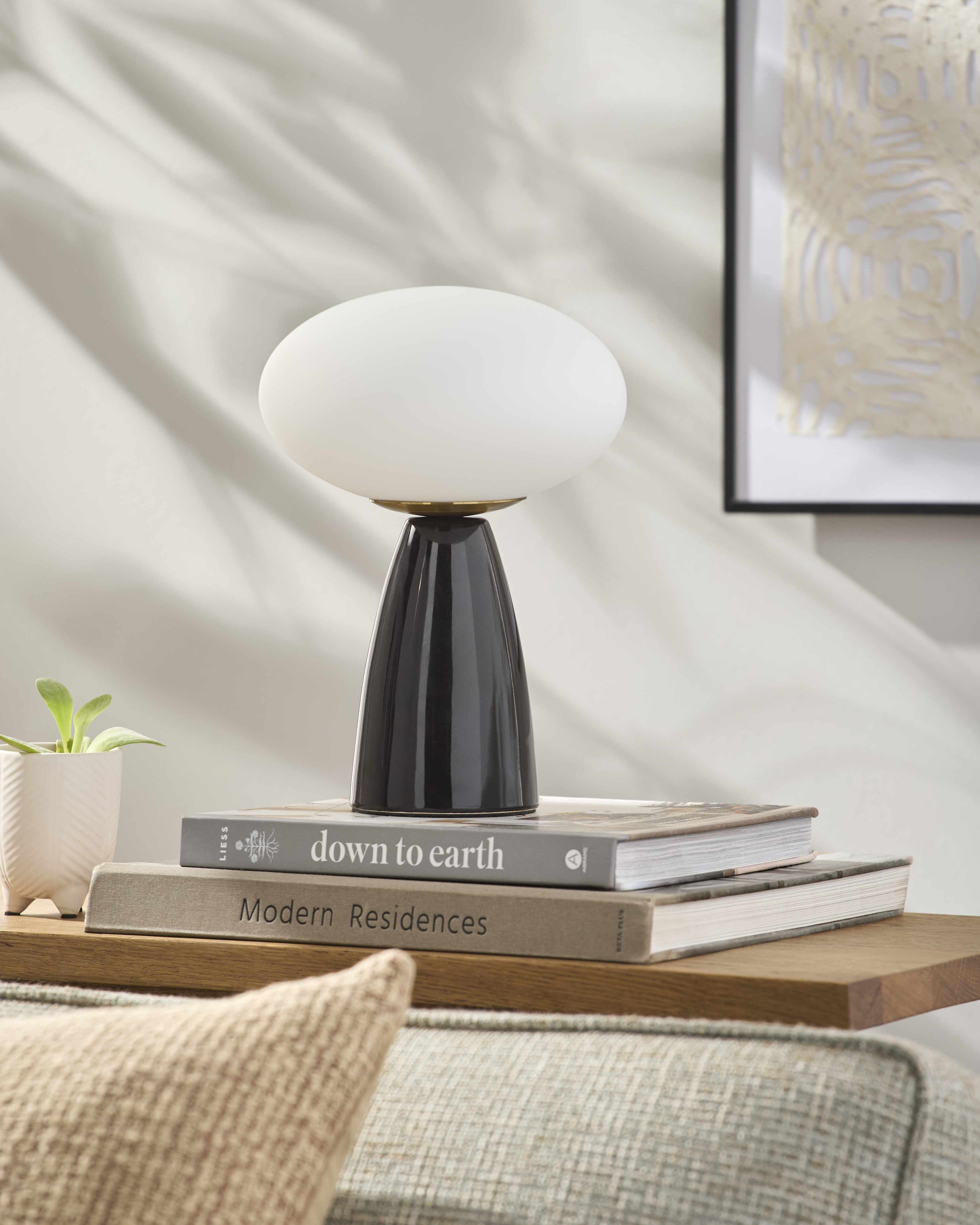 Contemporary table lamp with a black base and white shade on top of books on a wooden surface.