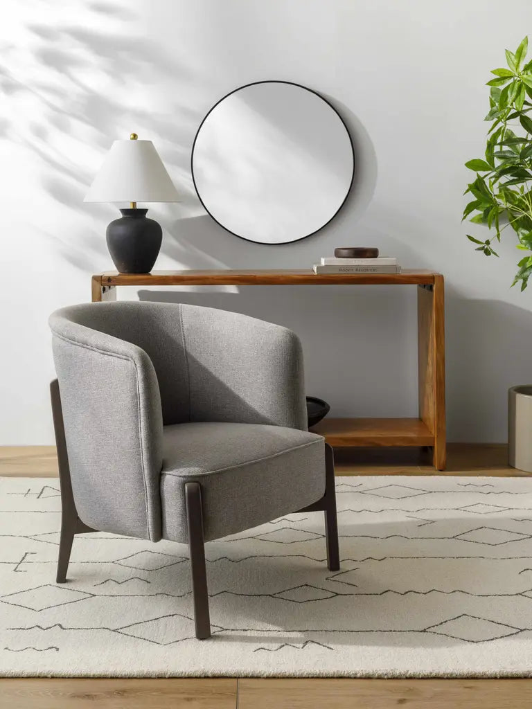 Gray armchair in a room with a wooden console table, mirror, and lamp.