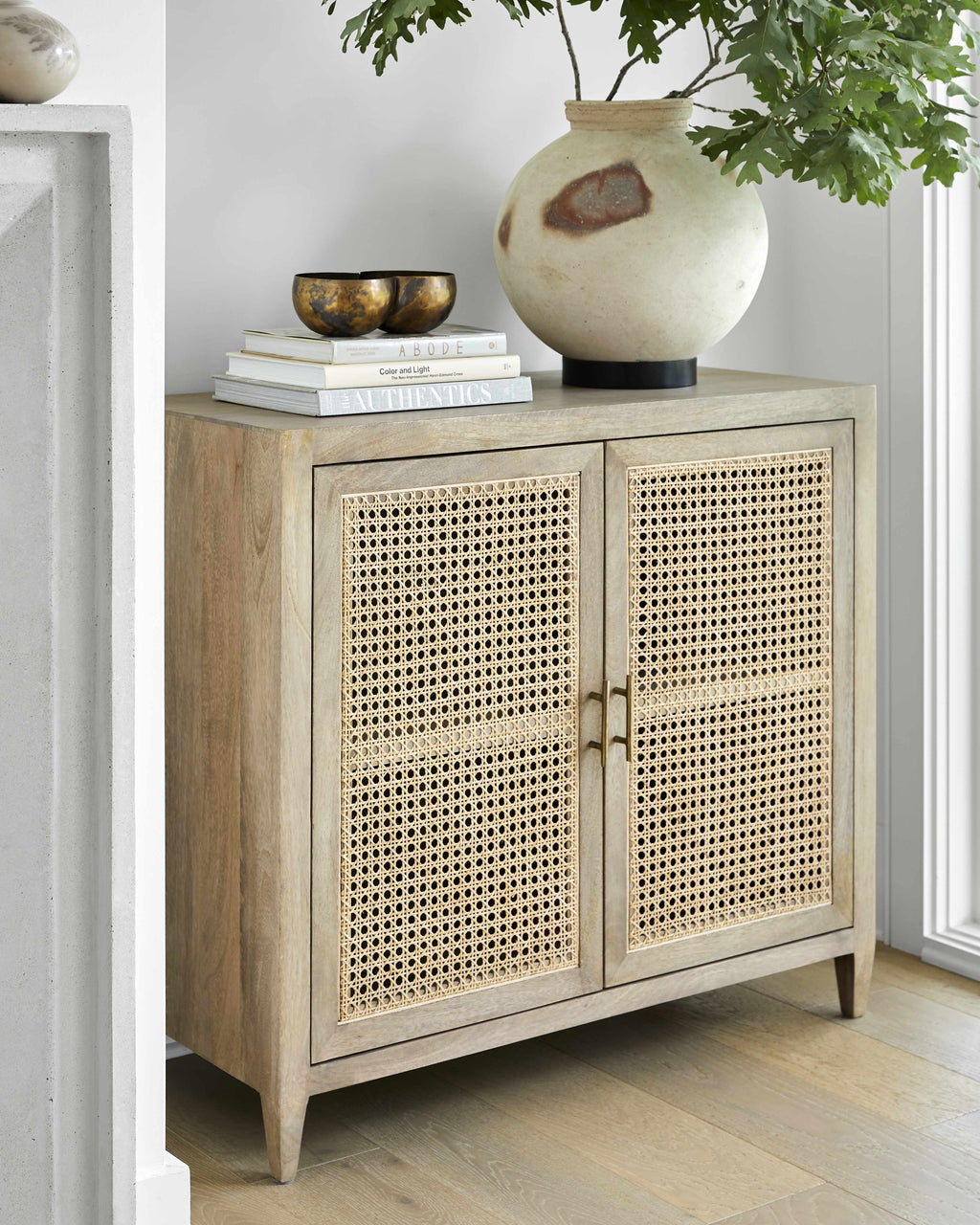 Mango wood modern cabinet with rattan doors in a room with a vase and books on top