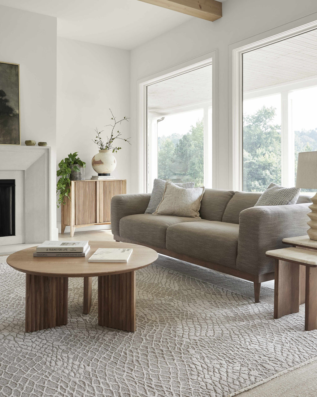 Modern living room with a gray sofa, wooden coffee table, and large windows.